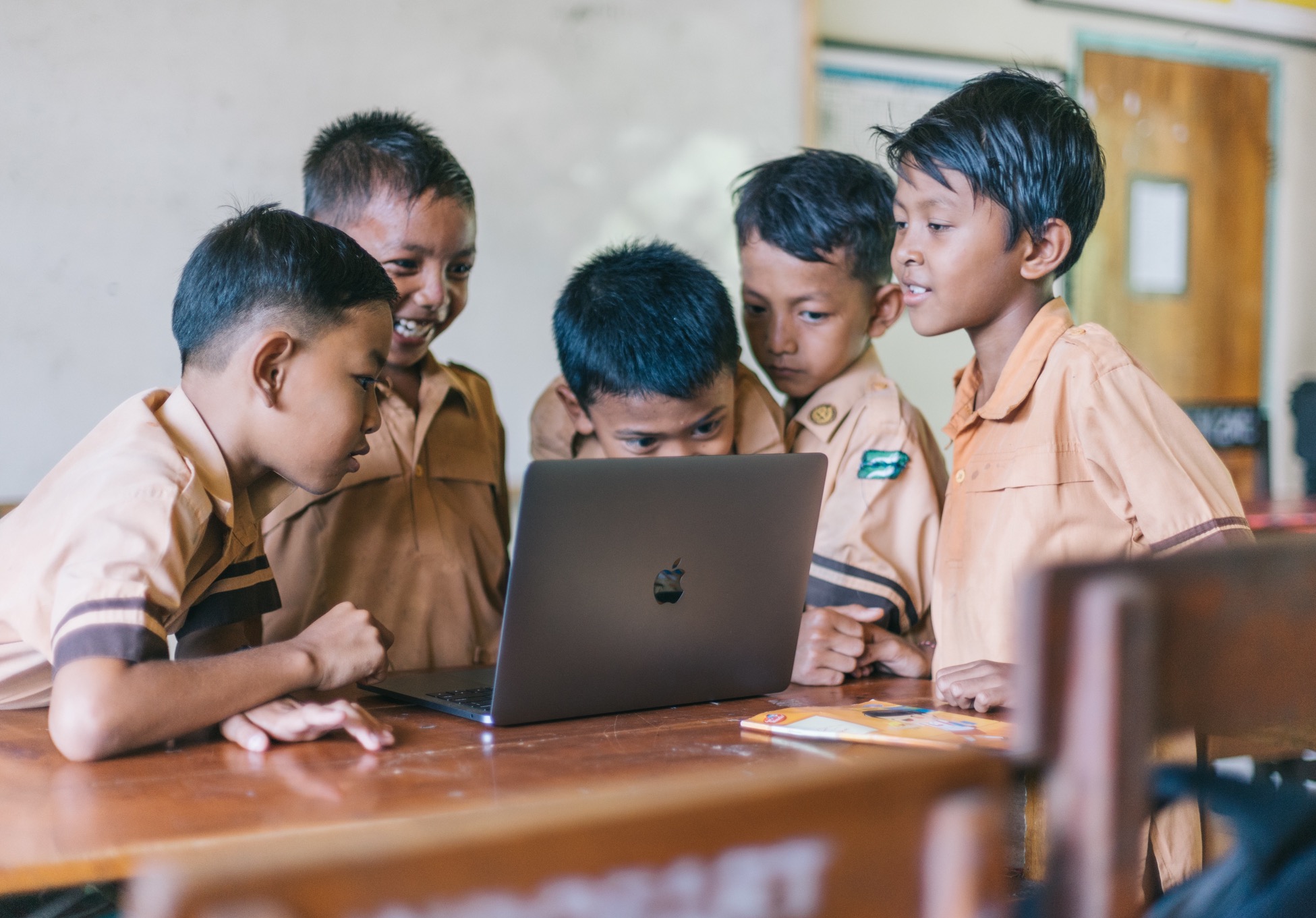 Classmates wearing uniforms standing around and looking at a laptop together